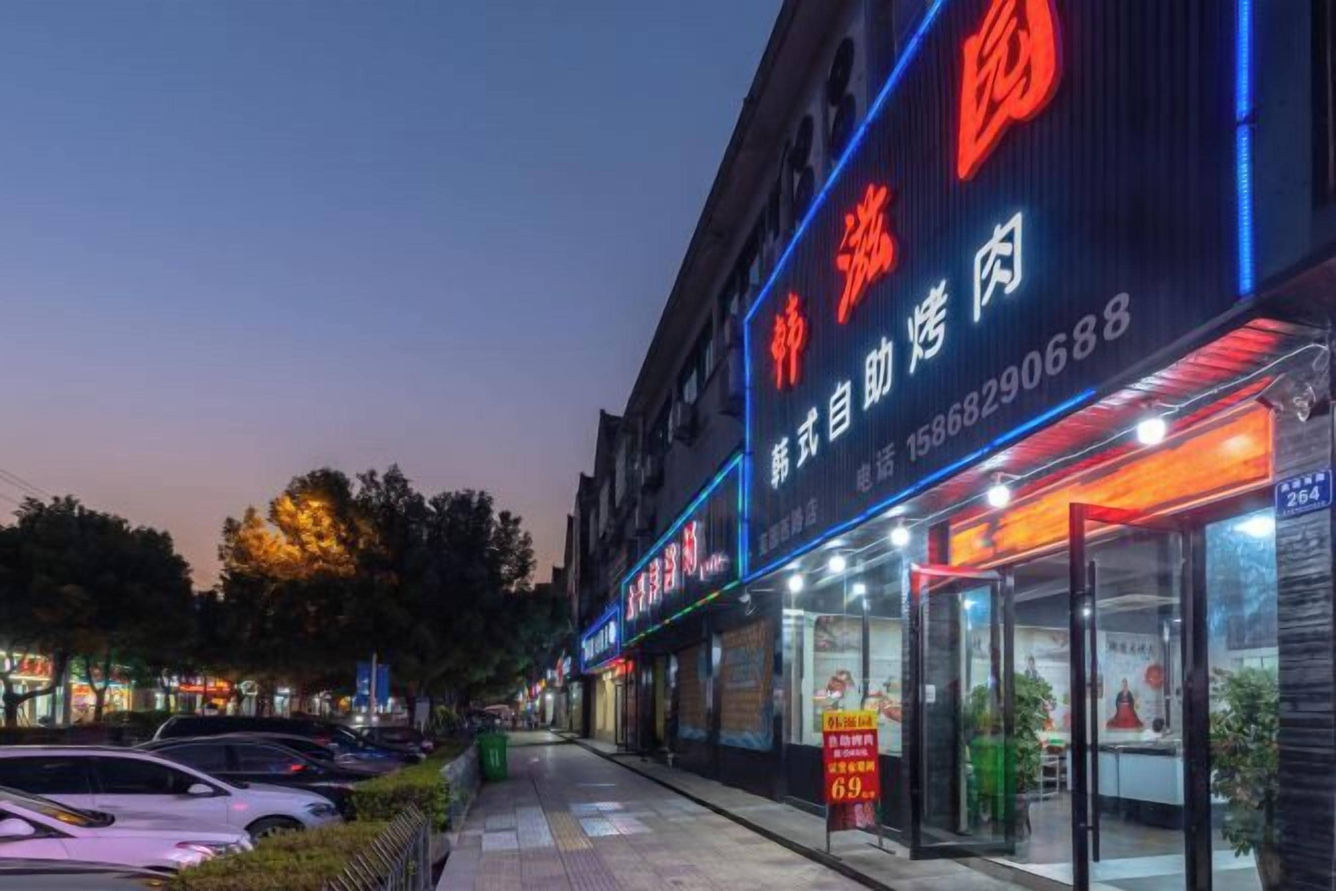 A building with illuminated signage, a storefront, and a sidewalk with parked cars.