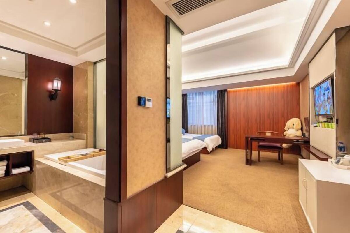 Habitación de hotel con un espejo grande, una bañera, una cama, un escritorio y una silla.