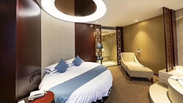 A hotel room with a large bed, a sitting area, a desk, and a bathroom.