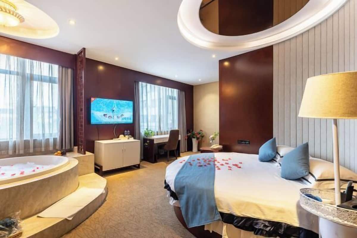 Una habitación de hotel con una cama grande, una zona de estar con escritorio, televisión y bañera.