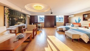 A hotel room with a TV, a dining area, a sofa, a bed, and a view of the city.
