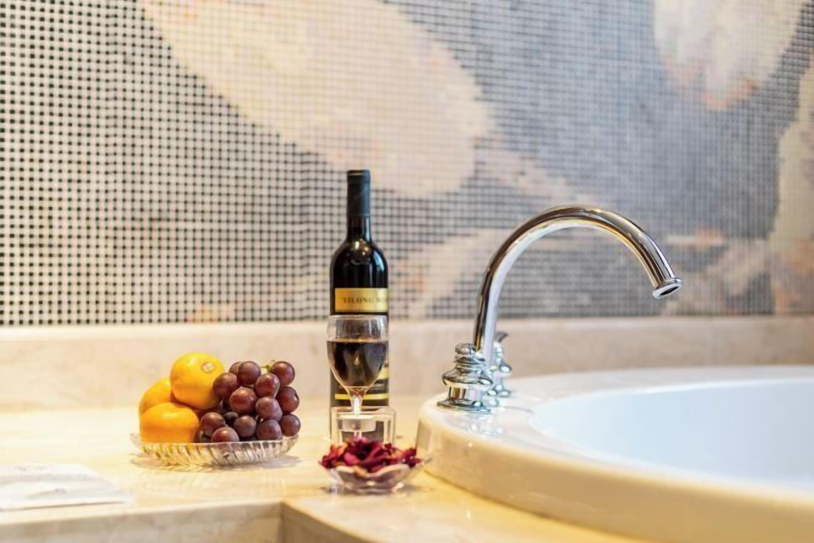 A bathroom sink with a bottle of wine and a bowl of fruit.