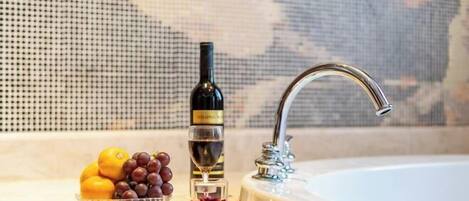 A bathroom sink with a bottle of wine and a bowl of fruit.