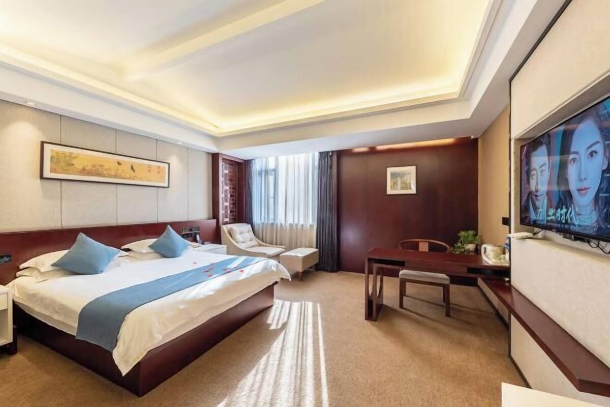 Una habitación de hotel con una cama grande, un escritorio, una silla, un televisor y obras de arte en las paredes.