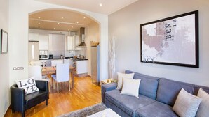 A modern living room with a grey sofa, a black armchair, and a coffee table. A kitchen is visible in the background with white cabinets and a dining area. - Apartment in Barcelona near Seabeach (Barcelona)