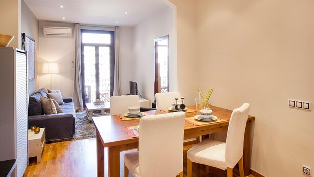 A modern living room with a sofa, a dining table with chairs, a lamp, and a TV. - Apartment in Barcelona near Seabeach (Barcelona)