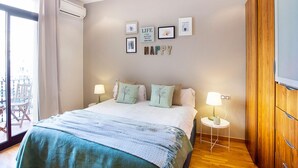 Een slaapkamer met een bed, twee nachtkastjes, een wandtelevisie en een balkon met een stoel.