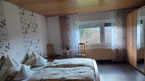 Un dormitorio con techo de madera, una cama grande con ropa de cama estampada, una mesita redonda con una silla y una ventana con persianas.