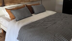 Un dormitorio con cama, ropa de cama blanca, una colcha a cuadros y una viga de techo de madera.