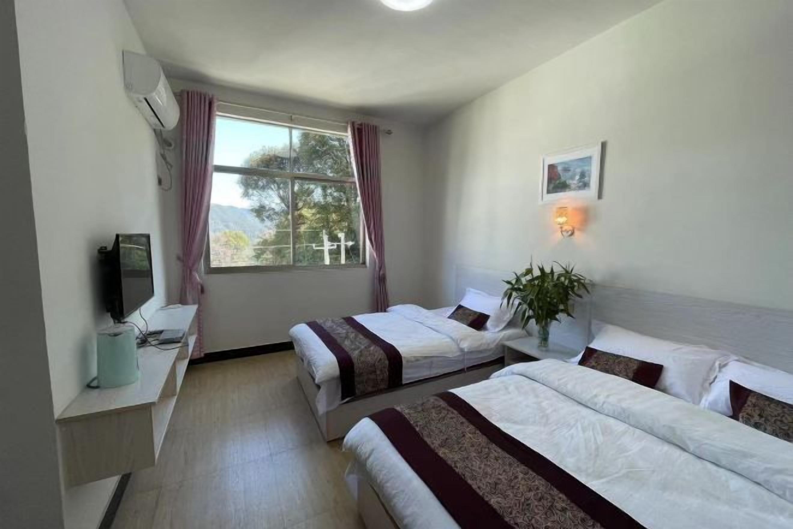 A hotel room with two beds, a TV, a desk, and a window with curtains.