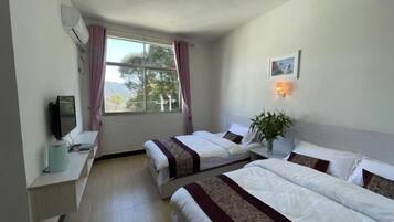 A hotel room with two beds, a TV, a desk, and a window with curtains.