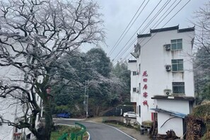 A residential street with a white building, a tree with bare branches, and a blue object on the ground. - Huatianju Inn, Jiangling, Wuyuan (Wuyuan)