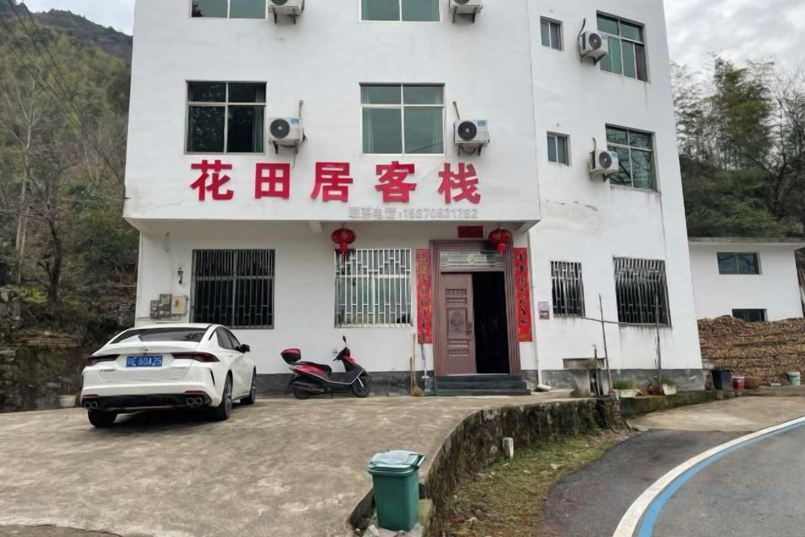 A two-story building with a red sign indicating a guesthouse. There are air conditioning units on the exterior, a parked car, and a motorcycle.
