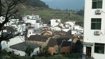 A village with traditional white buildings, a modern building with air conditioning units, and a hilly landscape in the background.