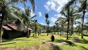 Un complexe hôtelier tropical doté d’une pelouse verdoyante, de palmiers et d’un petit bâtiment surmonté d’un toit rouge.