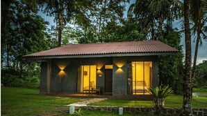 Une petite maison de plain-pied, dotée d’un toit en pente, de grandes fenêtres et d’un porche avec deux chaises.