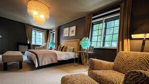 A hotel room with a large bed, a zebra-patterned armchair, a small table with a lamp, and a view of greenery through the windows. - Hakuba Mountain Lodge (Hakuba)