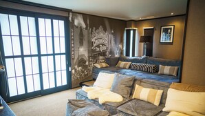 A modern living room with a sectional sofa, a large window with a view, and a cinema-themed mural on the wall. - Hakuba Mountain Lodge (Hakuba)