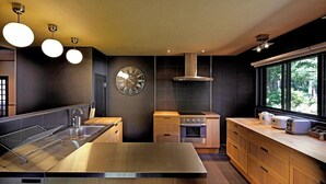 A modern kitchen with a central island, stainless steel appliances, wooden cabinets, and a large window providing a view of greenery. - Hakuba Mountain Lodge (Hakuba)