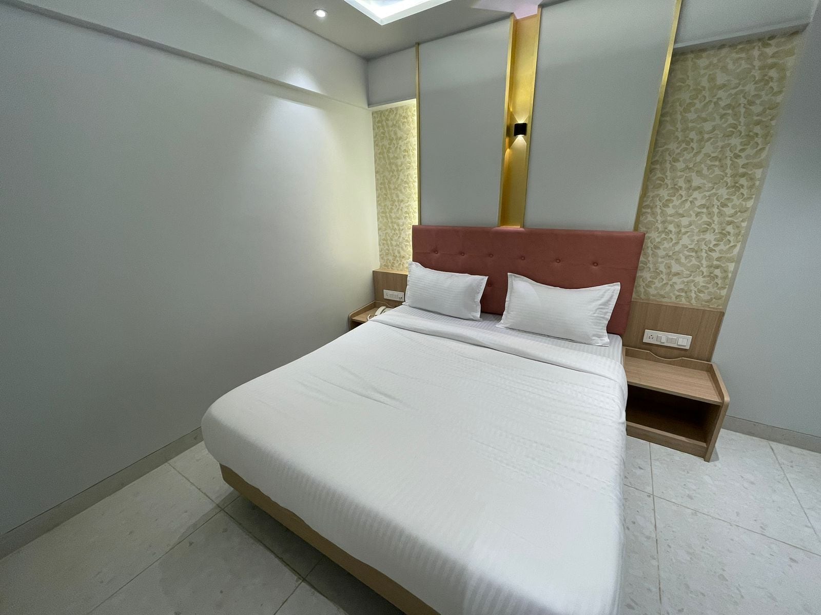 A neatly made bed in a hotel room with a modern design, including a headboard with vertical gold accents and a patterned wallpaper on the adjacent wall.