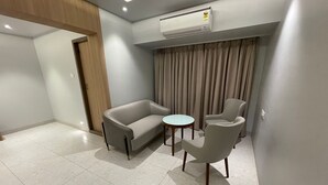A modern, well-lit room with a sofa, two armchairs, a small round table, and a ceiling-mounted air conditioning unit. - Hotel The West Coast (Vasai)