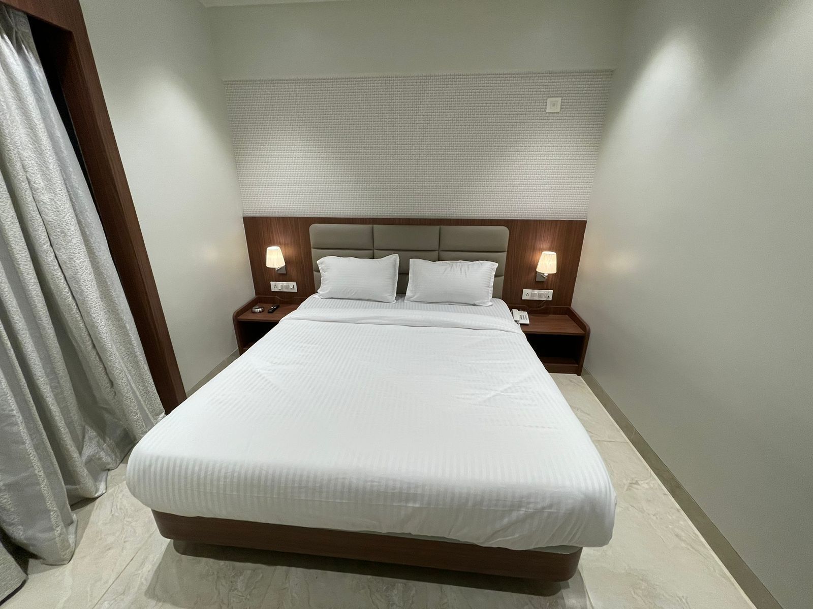 A neatly made bed with white linens, two bedside tables with lamps, and a headboard with a textured panel.