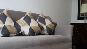 Un divano grigio con due cuscini decorati e un tavolino laterale in legno scuro.