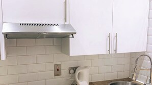 Una cucina moderna con mobili bianchi, una cappa aspirante in acciaio inossidabile, forno a incasso, piano cottura a induzione nero, bollitore bianco e lavello in acciaio inossidabile.