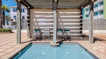 A pool area with a covered seating area, a sign indicating kiddie pool rules, and a wooden fence.