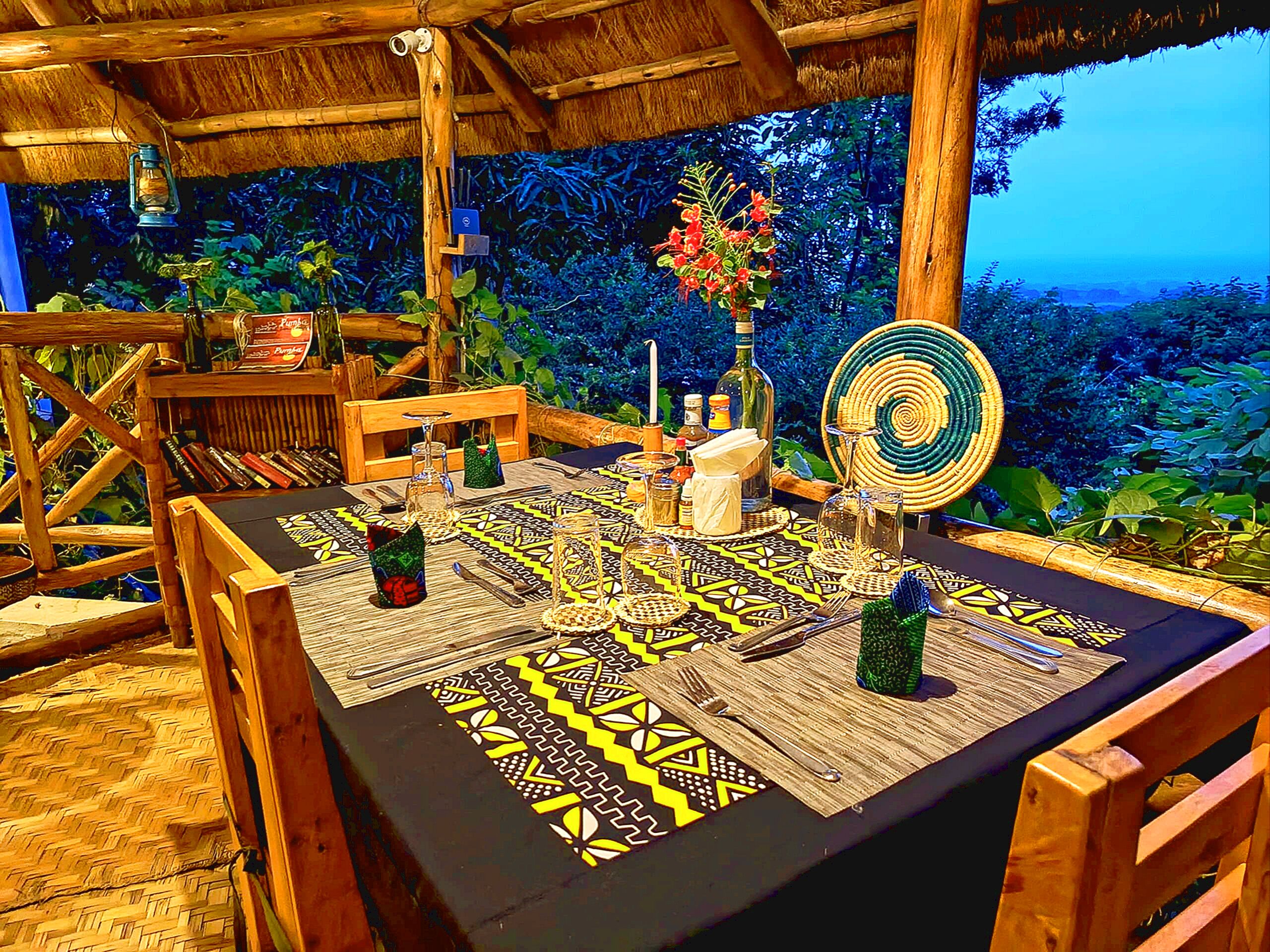 A table set with a patterned tablecloth, wooden chairs, and a tropical backdrop.