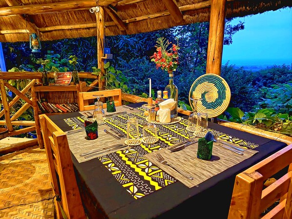 A table set with a patterned tablecloth, wooden chairs, and a tropical backdrop. - Pumba Safari Cottages (Kichwamba)