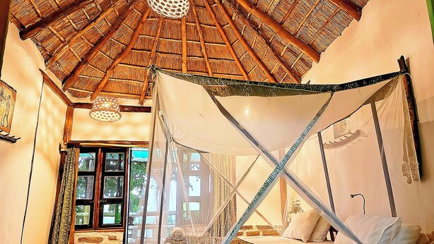 A room with a four-poster bed, a thatched roof, and a view of the outside. - Pumba Safari Cottages (Kichwamba)