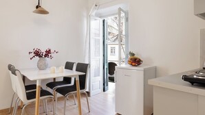 Une cuisine moderne avec une table à manger, des chaises, un réfrigérateur et une vue sur l’extérieur grâce à une porte ouverte.