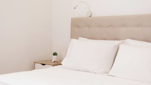 Un lit bien fait, avec du linge de lit blanc et une tête de lit, une table de chevet avec une lampe et une petite plante en pot.