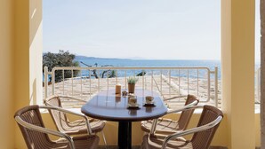 A balcony with a table and four wicker chairs, overlooking a beach and the sea.