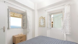 A bedroom with a bed, a wooden dresser, a window with a view, and a mirror.