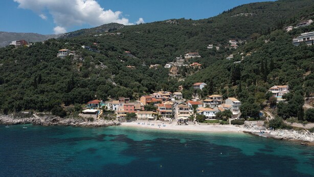 A coastal town with buildings on a hillside, a beach, and clear blue waters.