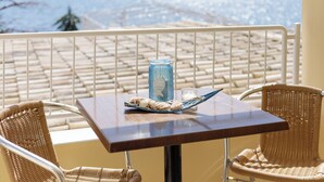 Un balcon avec des fauteuils en osier, une table, une bouteille bleue et un verre.