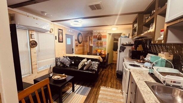 Una cocina compacta con estufa, lavamanos y armarios. Hay un comedor con una mesa y sillas.