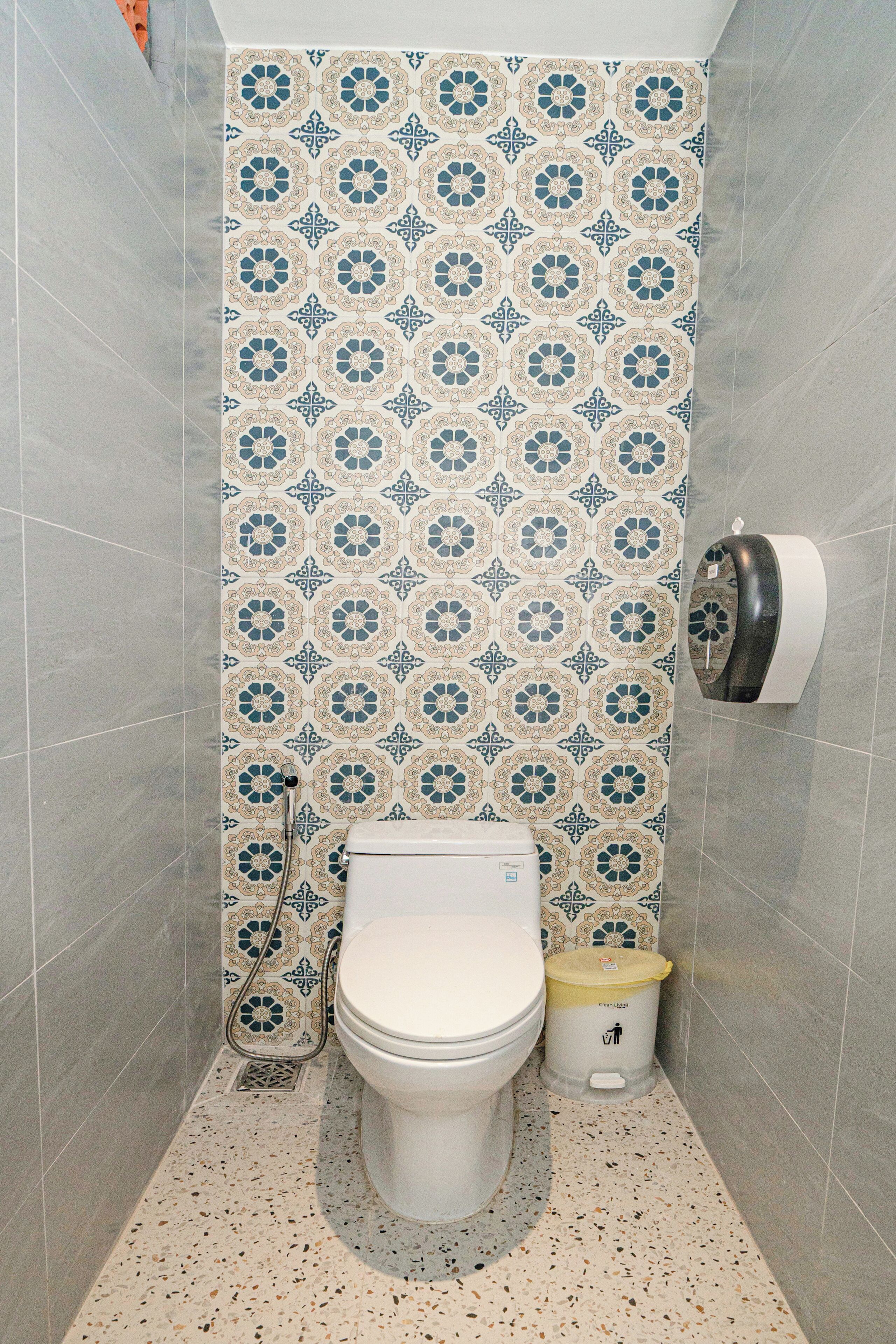 A small bathroom with a toilet, a trash bin, and a paper towel dispenser.