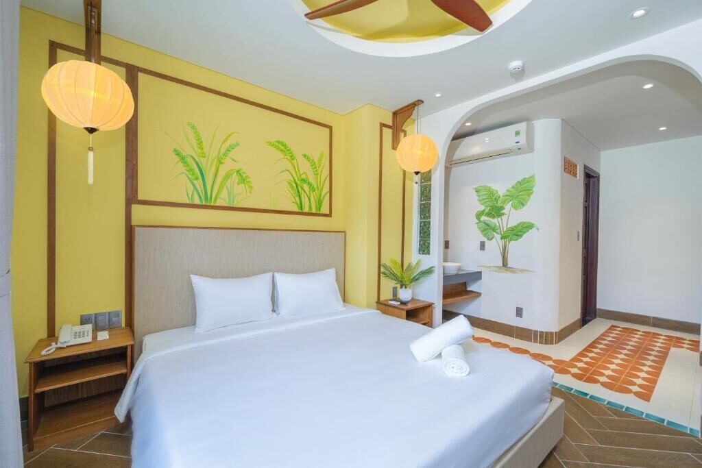 A hotel room with a bed, bedside tables, a phone, a plant, and a wall with a plant mural.
