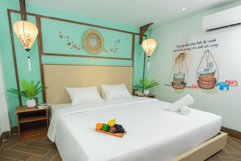A neatly made bed with a fruit tray, a wall with decorative wall art, and a bedside table with a lamp.