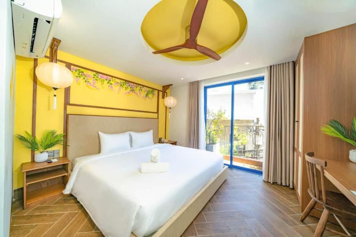 A hotel room with a large bed, a ceiling fan, a balcony with a view, and a wooden desk.