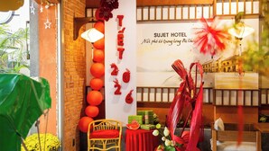 A hotel reception area with a brick wall, red lanterns, a wooden chair, a table with gifts, and a sign reading "SUJET HOTEL". - Sujet Hotel Da Nang (Da Nang)
