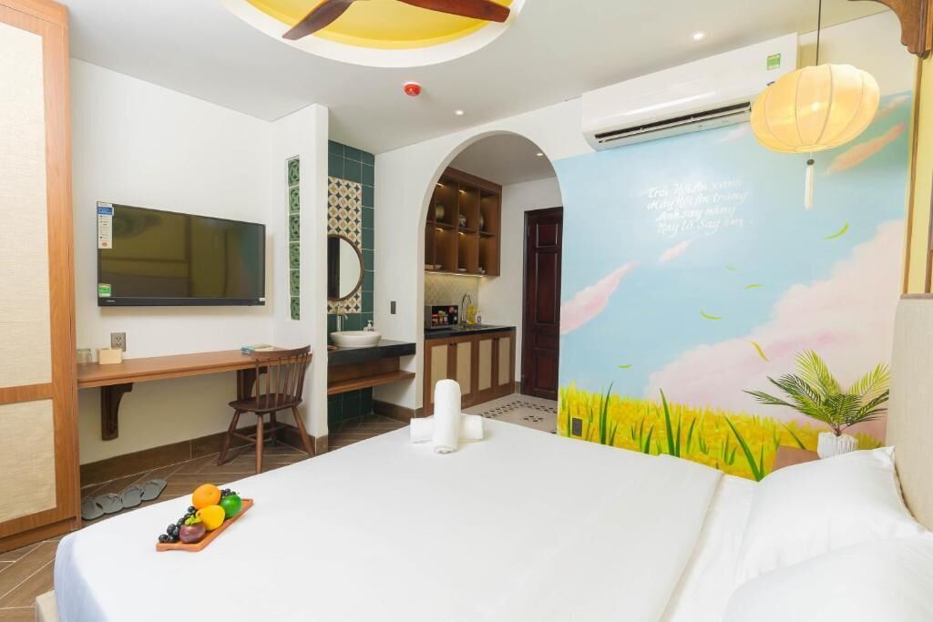 A bedroom with a bed, a desk, and a TV. There is a bathroom with a sink and a shower. The room has a mural on the wall.
