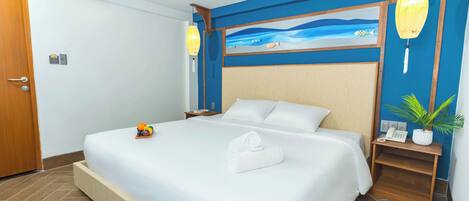 Una habitación de hotel con una cama grande, un cuadro de una playa en la pared, una mesita de noche de madera con un teléfono y una planta en maceta.