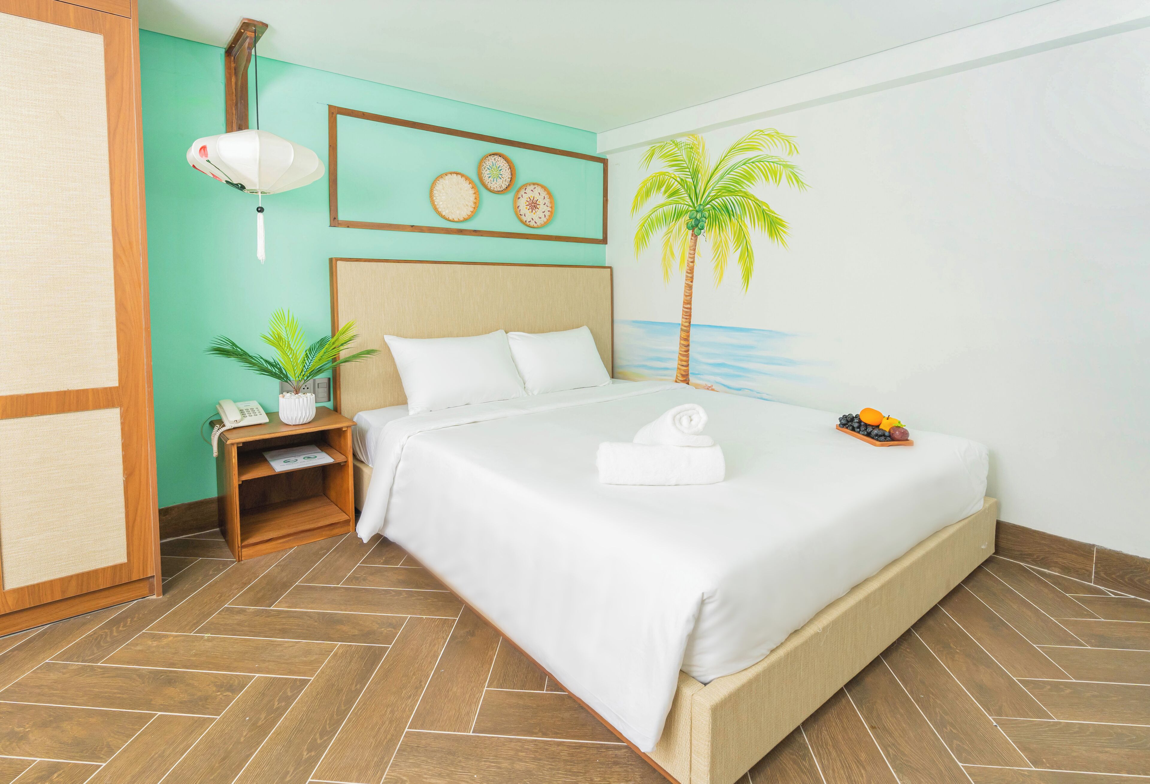 A neatly made bed with white linens, a bedside table with a lamp, a wall-mounted telephone, and a small potted plant.