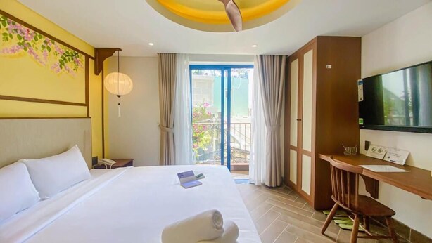 A hotel room with a bed, a desk, a television, and a balcony with curtains. - Sujet Hotel Da Nang (Da Nang)