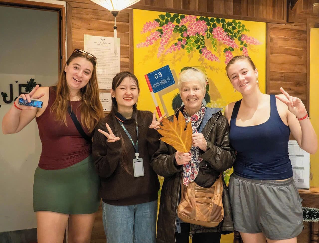 Un groupe de personnes se tient à l’intérieur, devant un mur en bois et sur fond d’un tableau jaune.