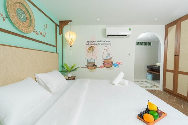 A hotel room with a bed, a wall decoration, a small table with fruits, and a potted plant. - Sujet Hotel Da Nang By Haviland (Da Nang)
